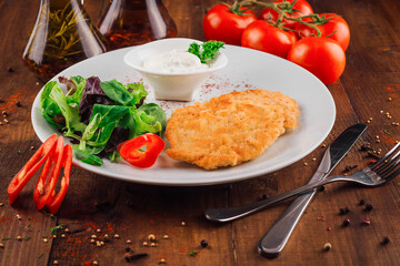 Breaded chicken breast served with salad and sauce on white plate