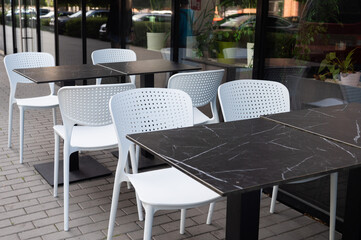Outdoor cafe seating with white plastic chairs and black marble tables.
