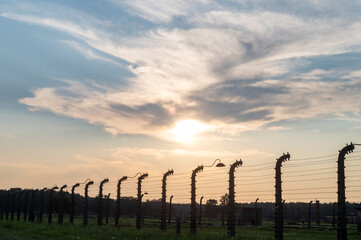Obraz premium Sunset view of barbed wire fence with dramatic clouds in the sky.
