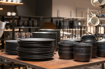 Stack of black plates and bowls displayed on a wooden table in a kitchenware store.