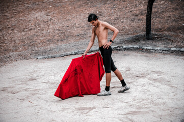 Front view of a young adult bullfighter practicing performance holding his red cloak with one hand