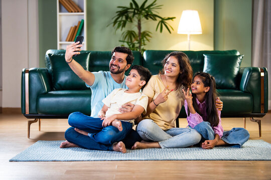 Happy Indian family taking a selfie while sitting on the floor, enjoying new apartment life