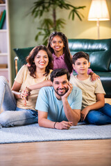 Happy Indian family enjoying quality time at home with father on floor, kids sitting on his back