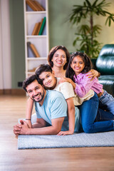 Happy Indian family enjoying quality time at home with father on floor, kids sitting on his back