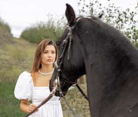 Obraz premium beautiful,delicate woman in white dress posing with black scary dark horse. girl and animal in orchard in garden.female is trying to pet the horse.