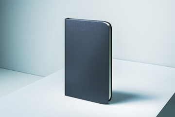 Empty closed black notebook with mock up place on light desk and concrete wall background background. Back to school, education and supplies concept. 3D Rendering.