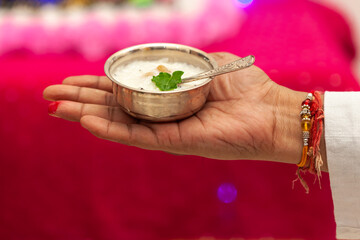 Man presenting panchamrit in a silver bowl with a spoon, preparing for 'Krishna Janmashtami'...