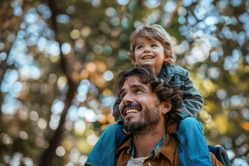 Portrait of happy father giving son piggyback ride on his shoulders and looking up. Cute boy with dad playing outdoor