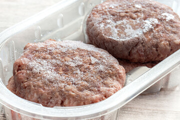 Frozen beef burgers in plastic tray packaging thawing.  On a grey wood background