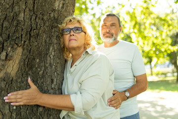 Obraz premium Senior couple hugging tree enjoying sunny day in park