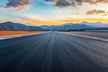 Naklejka premium Empty race track is disappearing into the distance at sunset with mountains background. High quality photo