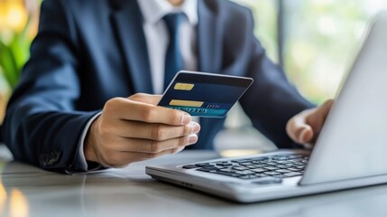 A businessman processes an online payment using a credit card while seated at a modern workspace during daylight hours