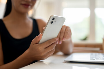 A woman working remotely from a coffee shop, checking reading messages on her smartphone.