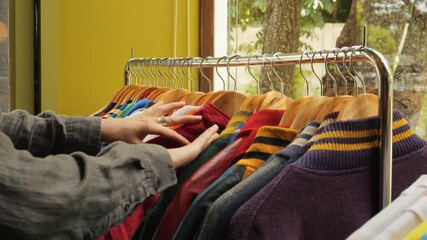 Female hands is picking out clothes from clothing rack in a vintage store, consumerism reduce reuse recycle concept. Chiang Mai, Thailand