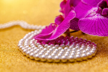 purple Orchid and pearl necklace on a shiny gold background

