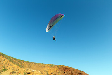 Paragliding against the backdrop of blue sky and red mountains