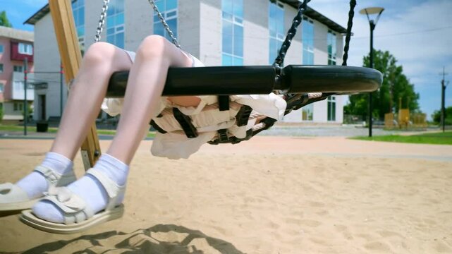 Little girl kid swinging on net swing in the park. Caucasian child swinging on playground. Cute child have fun in park. School girl play on swing. Slow motion