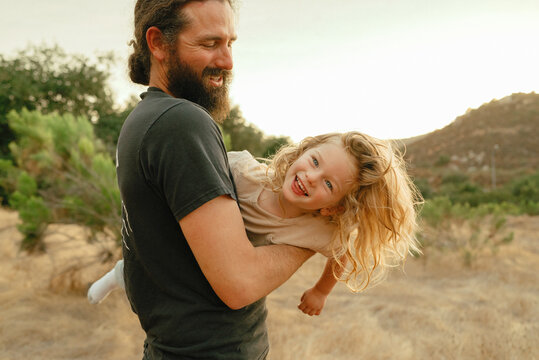 dad with beard and pony tail swings around child in mountains