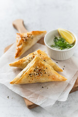 Triangle filo pastry savory pies served with tzatziki dip on wooden board, Greek stuffed food spanakopita for breakfast