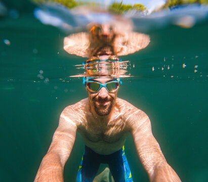 Happy man in swimming goggles taking selfie underwater