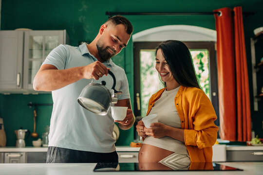 Pregnant woman with husband pouring tea in cup at home