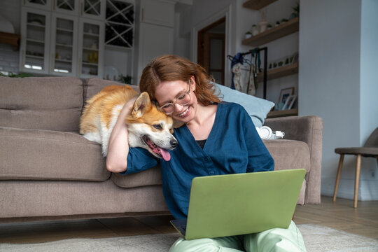 Smiling woman with laptop embracing pet dog at home