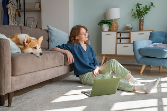 Contemplative woman with Welsh Corgi dog on sofa at home