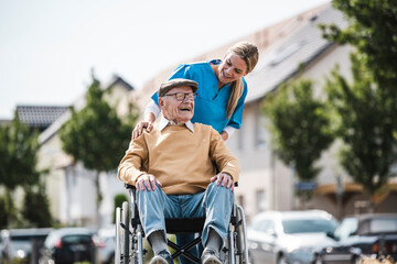 Happy elderly man sitting in wheelchair and talking with nurse
