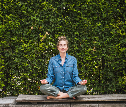 Portrait of woman meditating on bench in front of hedge