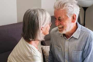 Elderly couple sitting on a cozy sofa, smiling and chatting with love and sweetness in their home. This heartwarming moment captures the essence of mature relationships, friendship, and the joy 