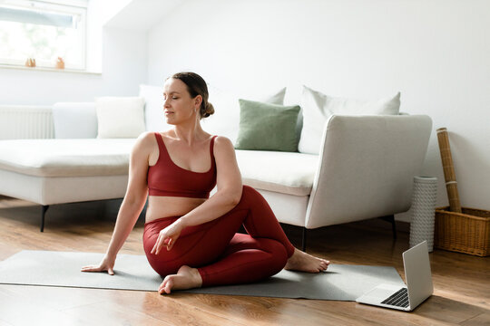 Woman with eyes closed practicing Paripurna Matsyendrasana pose on yoga mat at home
