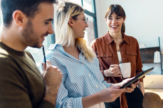 Happy businesswoman holding tablet PC and standing with colleagues in office