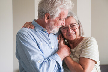 Portrait of a mature couple embracing each other in their home, posing affectionately for a photo in front of the camera. They share a loving glance after a lifetime together, smiling in casual 