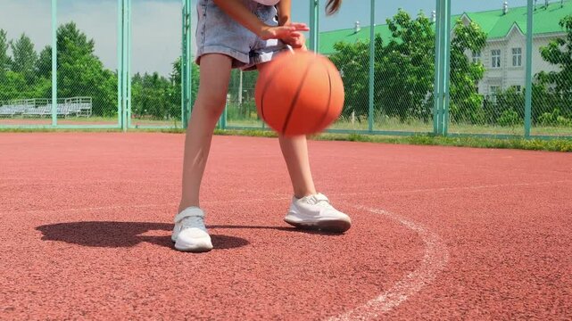 Girl bouncing basketball ball at outdoor court in park. Little kid practicing playing basketball with caring father. Sports leisure and weekend. Family time. Basketball game