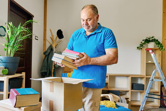 Senior man sorting books from box in new apartment