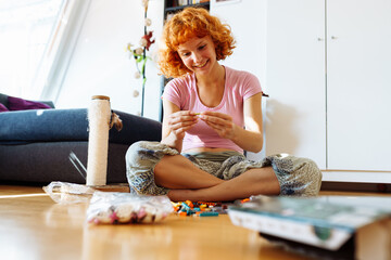 teenage girl assembles construction set according to instructions sitting on floor in room