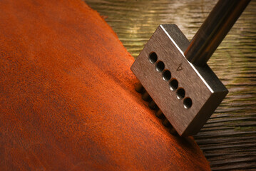 Leather hole puncher tool close up and leather on the tanner workbench concept background.