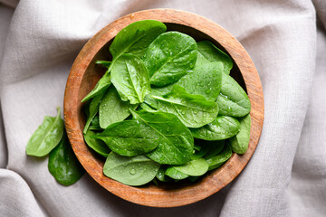 Baby spinach leaves with water drops in a wooden bowl on linen tablecloth. Raw organic spinach...