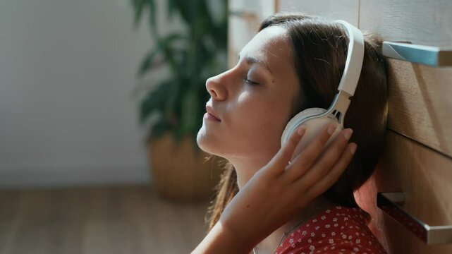 Woman listening music with headphones leaning on chest of drawers