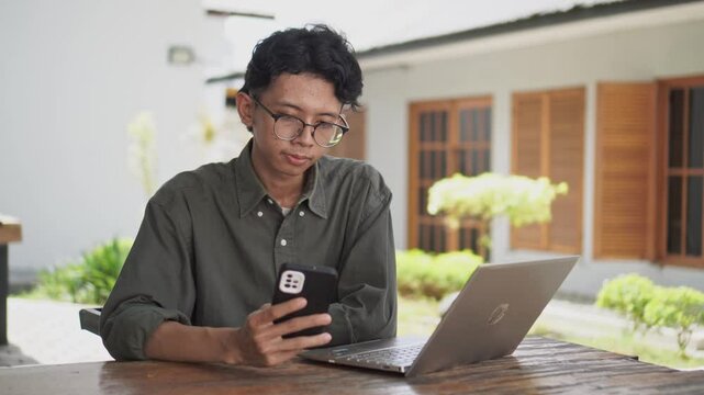 Outdoor shot of Asian man looking to his phone and laptop. man working at the cafe