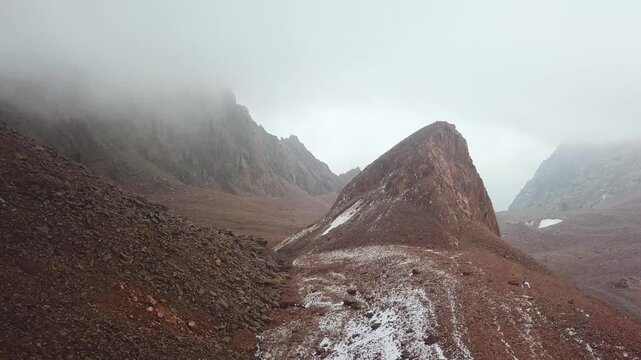 Foggy weather on the Talgar Pass in summer. Flight in the area of Bogdanovich glacier. Bare rocks high in the mountains, lack of vegetation