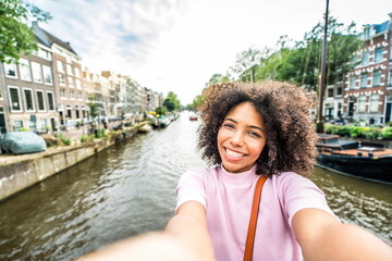 Happy female tourist visiting Amsterdam city, Netherlands - Cheerful young woman taking selfie picture walking in city street - Traveling, holidays and technology life style concept