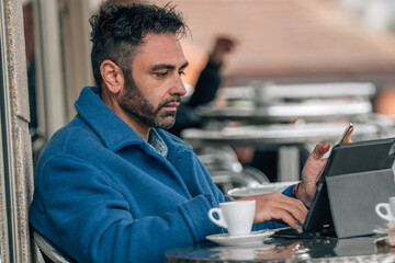 Fototapeta premium attractive young adult man with beard drinking coffee with mobile phone and tablet