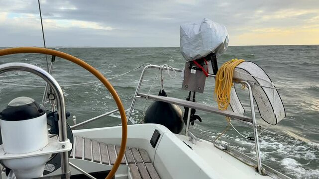 Rear view of sailboat with automatic steering tiller wheel at rough wind storm sea with outboard motor or engine and safety bouy mounted on stern riding waves