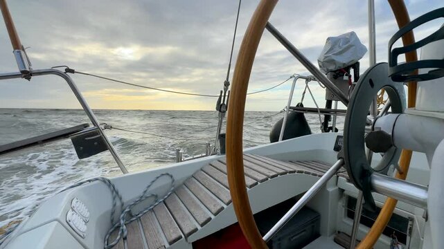 Rear view of sailboat with automatic steering tiller wheel at rough wind storm sea with outboard motor or engine and safety bouy mounted on stern riding waves