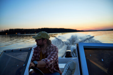 a man driving a boat on the river in the evening at sunset
