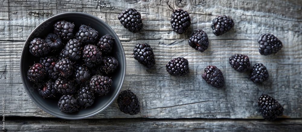 Poster Black raspberries arranged in a bowl on the left with a gray wooden table background on the right offering ample copy space image