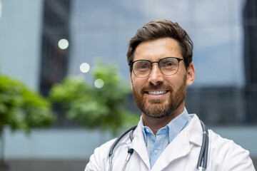 Smiling doctor in white coat with stethoscope outdoors, representing health, confidence, and medical expertise. Male medical professional showcasing friendly and approachable demeanor