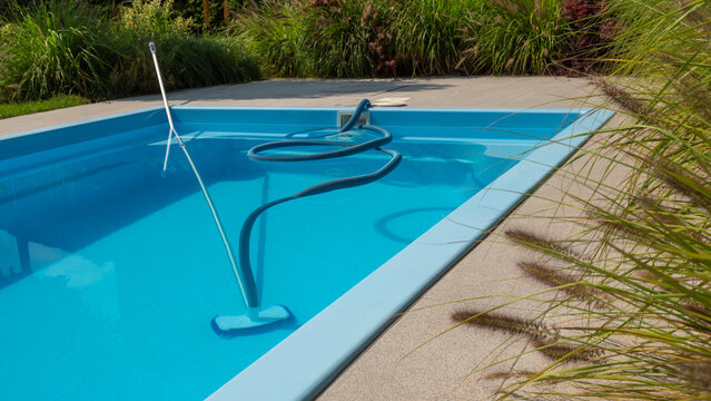 A pool cleaning hose and vacuum head in a clear blue pool, surrounded by greenery, emphasizing maintenance and cleanliness.