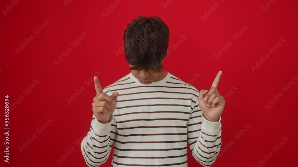 Canvas Prints Young hispanic man wearing stripes t shirt standing pointing up looking sad and unhappy, upset and indicating direction with finger, depressed over isolated red background